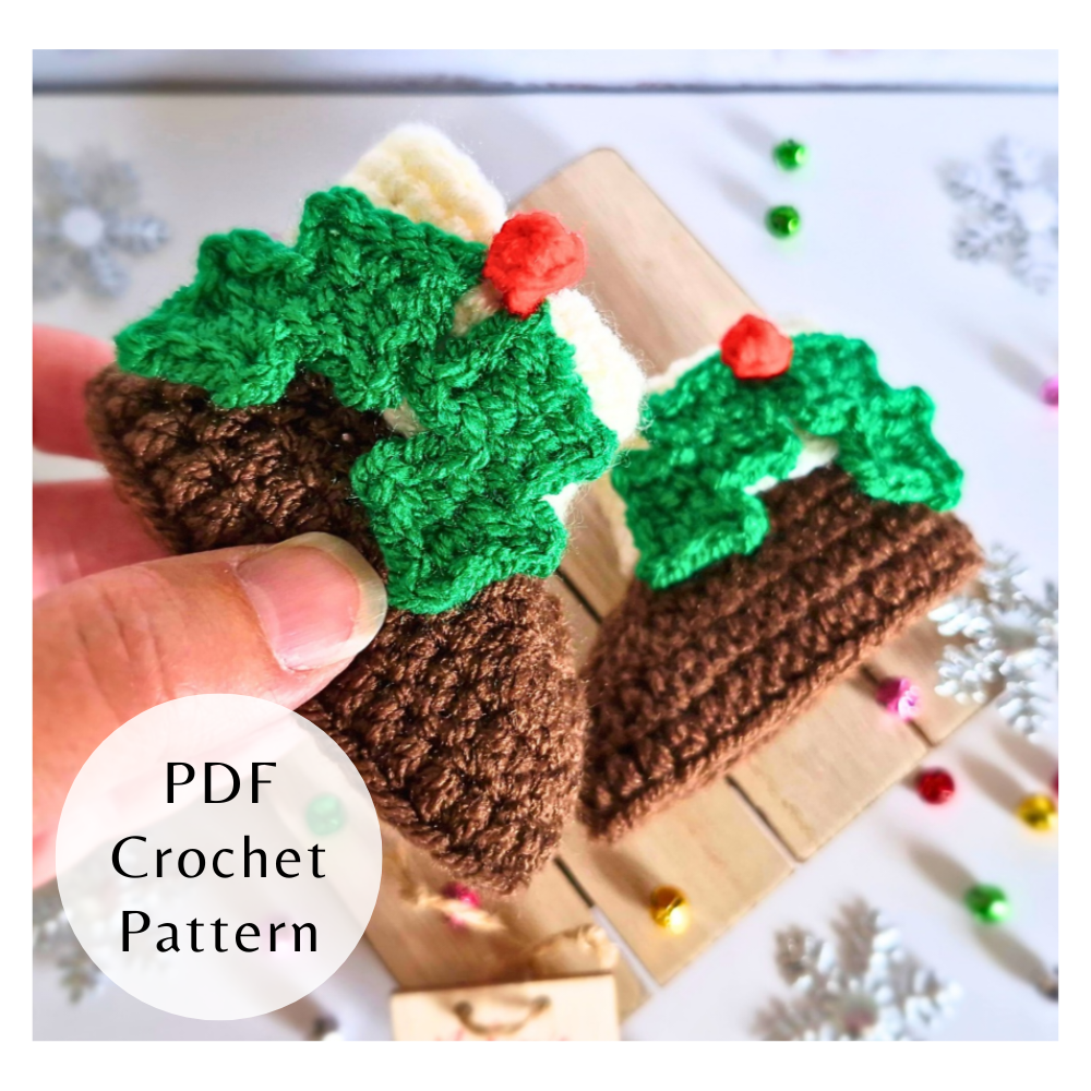 Hand holding a crocheted Christmas pudding ornament with green holly and red berry decoration