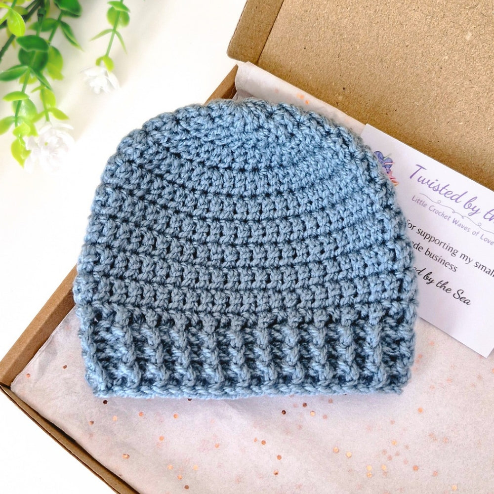 Blue crochet baby beanie on a box with a plant in the background