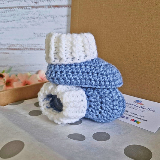 Blue and white crocheted baby booties on a polka dot surface with a business card in the background.