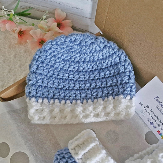 Blue and white crocheted baby hat on a textured surface with flowers in the background