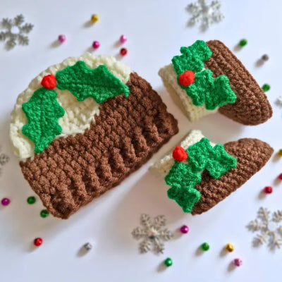 Crocheted Christmas pudding hat and booties with holly leaves and berries on a white background with decorative elements.