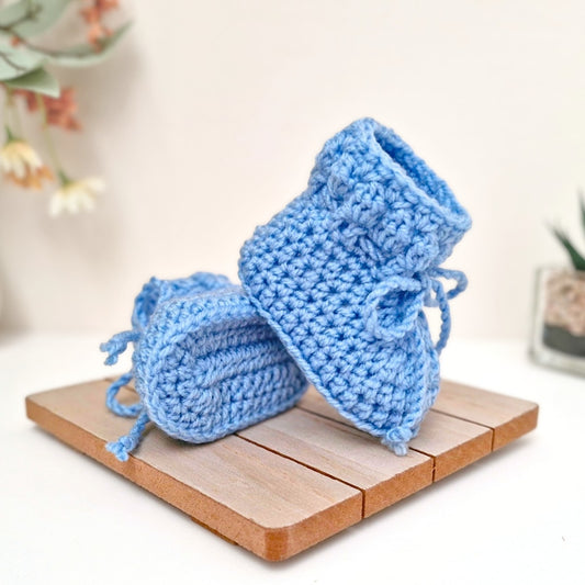 Pair of blue knitted baby booties on a wooden surface with a blurred background