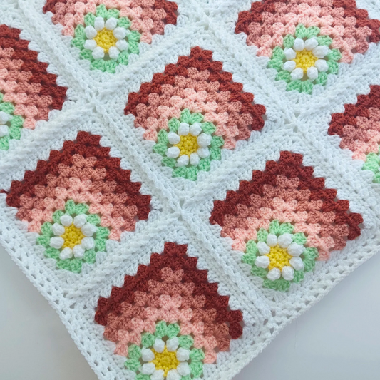 Crocheted blanket with diamond pattern and flower designs in red, pink, green, and yellow.
