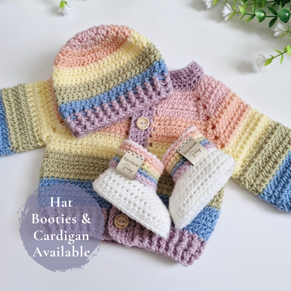A handmade crocheted baby outfit set featuring a striped hat, cardigan, and booties in pastel rainbow colors, arranged on a white surface with a decorative text overlay.