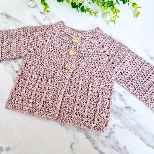 Neutral mushroom co.oured crochet baby cardigan with buttons on a marble surface