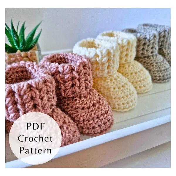 3 pairs of crocheted baby booties in various colours on a white surface with a plant in the background.