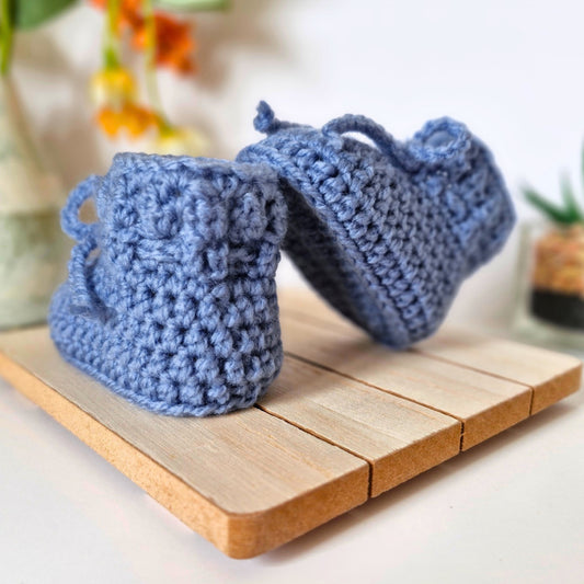 Blue crocheted baby booties on a wooden surface with a blurred background