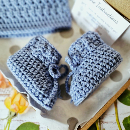 Blue crocheted baby booties on a textured surface with a blurred background