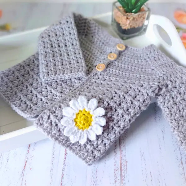 Handmade crochet baby cardigan with a daisy flower on a white surface