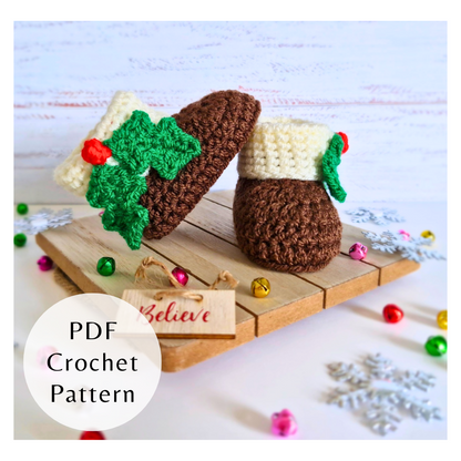 Crocheted baby booties with holly leaves and berries on wooden board surrounded by Christmas bells and snowflakes