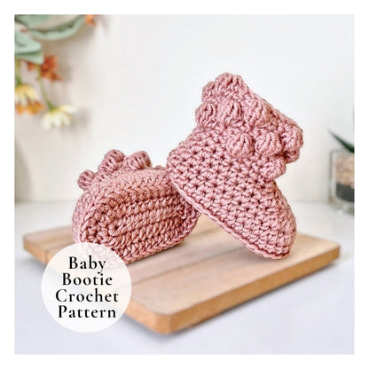Pink crochet baby booties on a wooden board with a blurred background