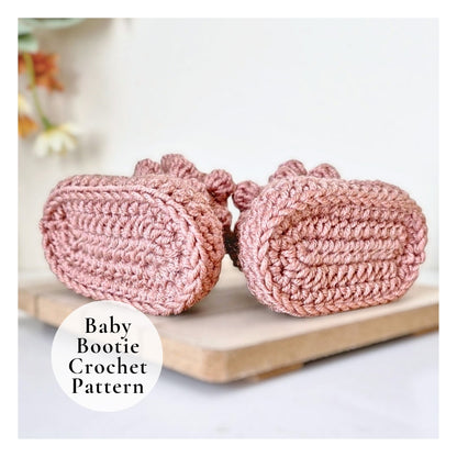 Pink crochet baby booties on a wooden board with a blurred floral background