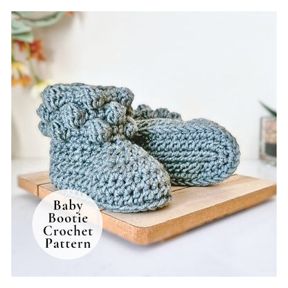Pair of blue crochet baby booties on a wooden board with a blurred background.