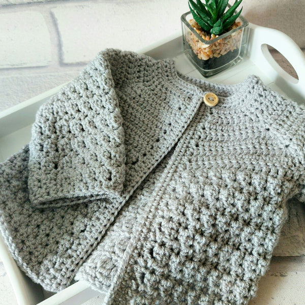 Handmade light gray crochet newborn baby cardigan with button on white tray and small succulent plant