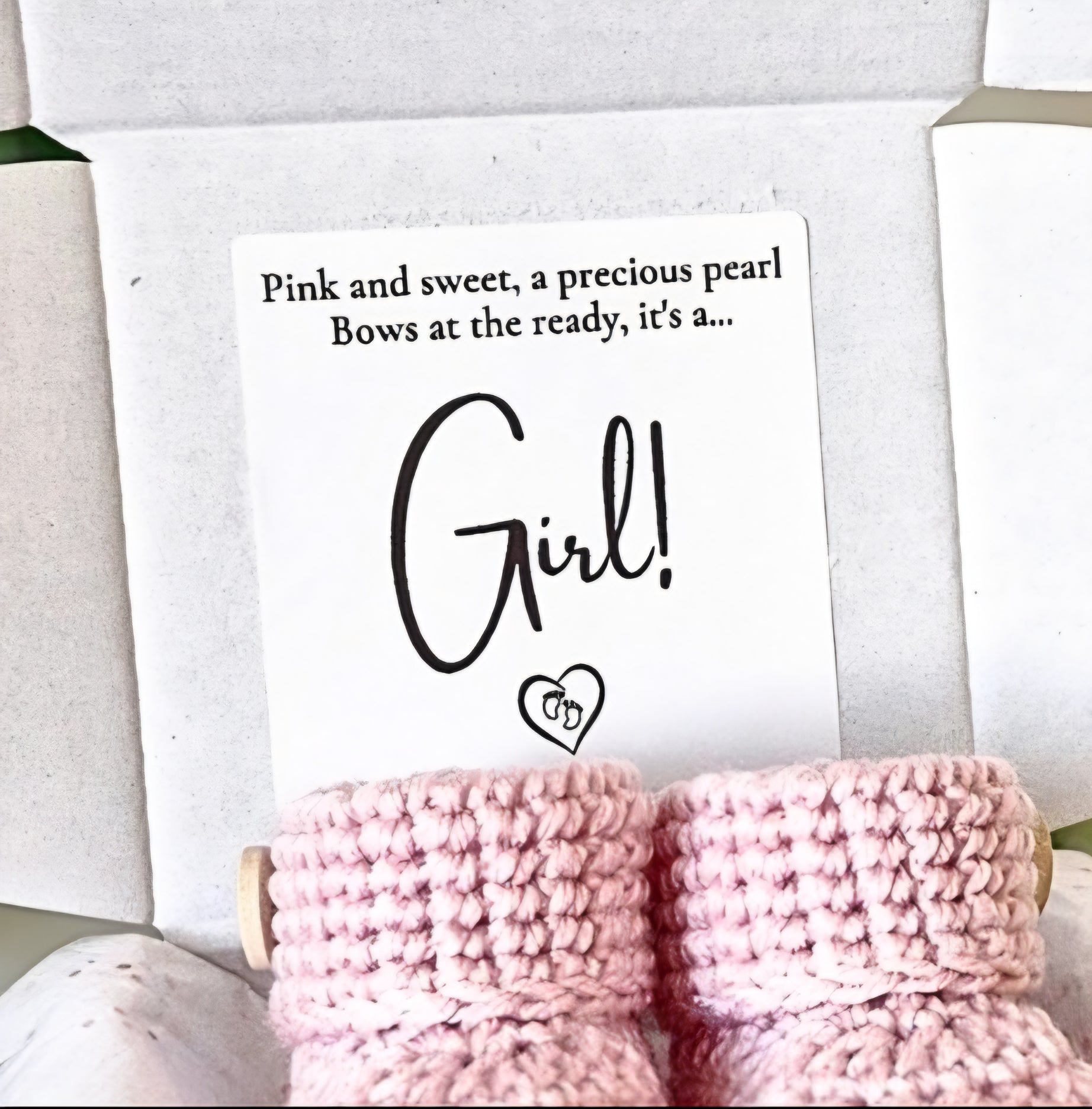 Pink baby booties with a sign announcing a girl, on a white background