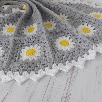 Grey crocheted blanket with white daisy flowers on a wooden surface
