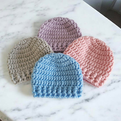 Four crocheted baby hats in different colors on a marble surface