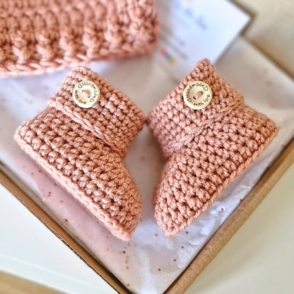Pair of milky tea coloured crochet baby booties with 'Handmade' label on a white background