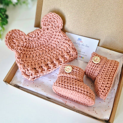 Crochet baby hat and booties gift set in a box with a card, against a light background. Shown in sie newborn and shade: milky tea