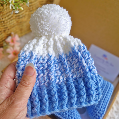 Blue and white crochet baby hat with a pom-pom held by a hand.