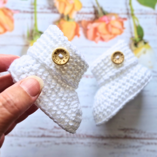 Handmade ‘Born in 2026’ Crochet Baby Booties – Handmade Newborn Gift or Pregnancy Reveal – Baby Booties crafted in soft acrylic yarn and available in multiple colours by Twisted by the Sea.