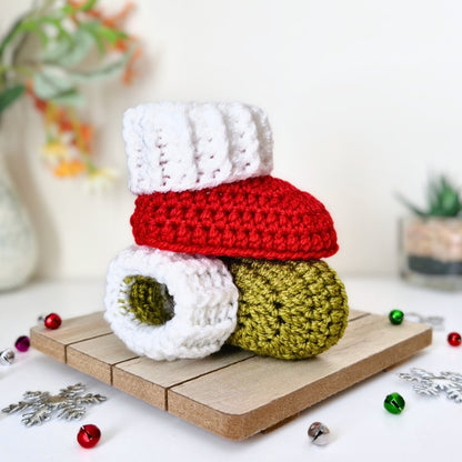 Two crocheted baby booties stacked on a small wooden tray, with Christmas decorations around them. 