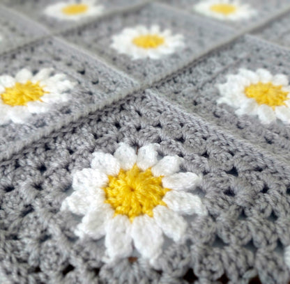 Gray crocheted blanket with white daisy flowers and yellow centers.