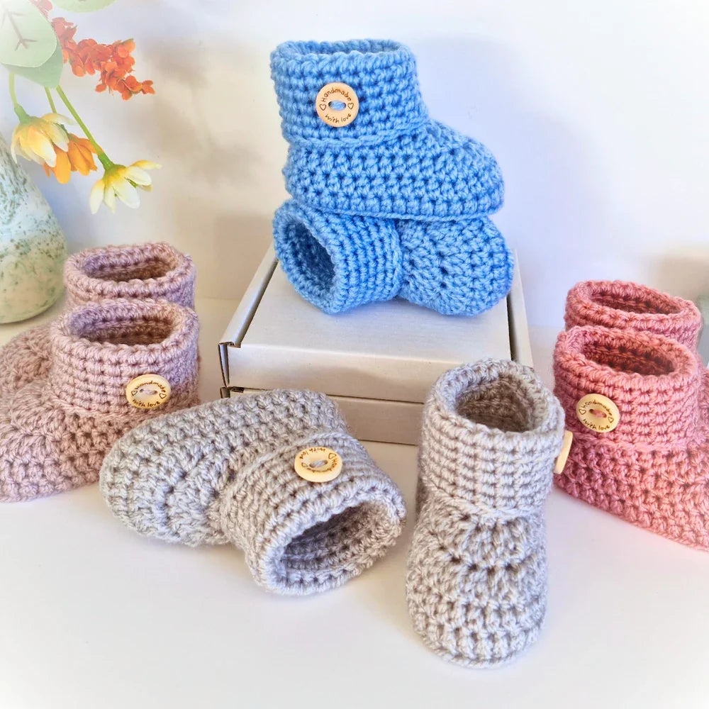 crochet baby booties featuring folded cuffs and a round wooden button engraved with "Handmade with Love" on a white background - Twisted by the Sea