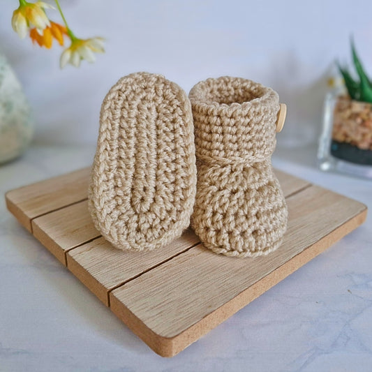 Pair of beige crochet baby boots on a wooden board with a light background
