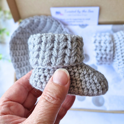 Hand holding a small gray knitted bootie with a blurred background