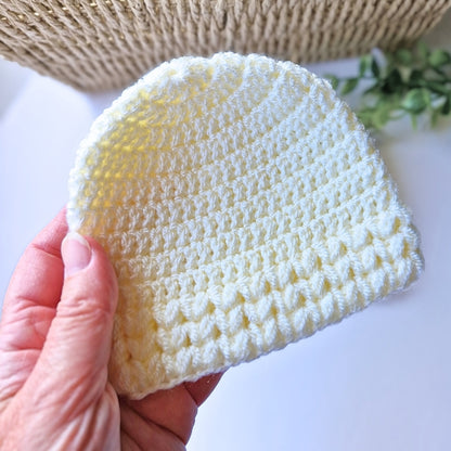 Hand holding a textured cream baby hat on a light background