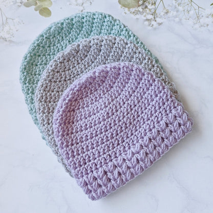 Three crocheted baby hats in pastel colors on a light background