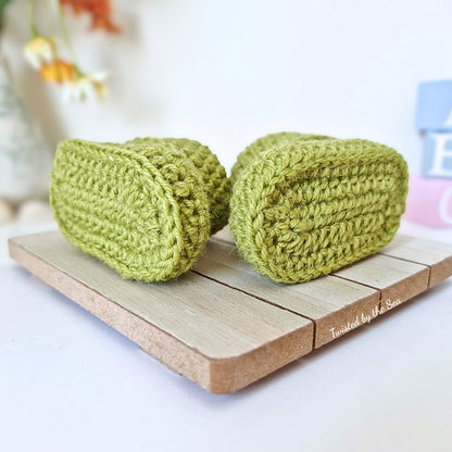 Sole view of Two green knitted booties on a wooden block with a blurred background