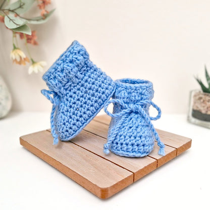 Pair of blue crochet baby booties on a wooden surface 