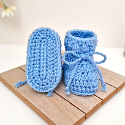 Pair of blue crochet baby booties on a wooden surface with a light background