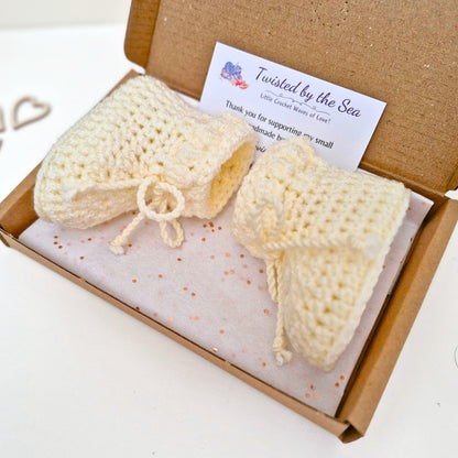 Knitted baby booties in a box with a label on a white background