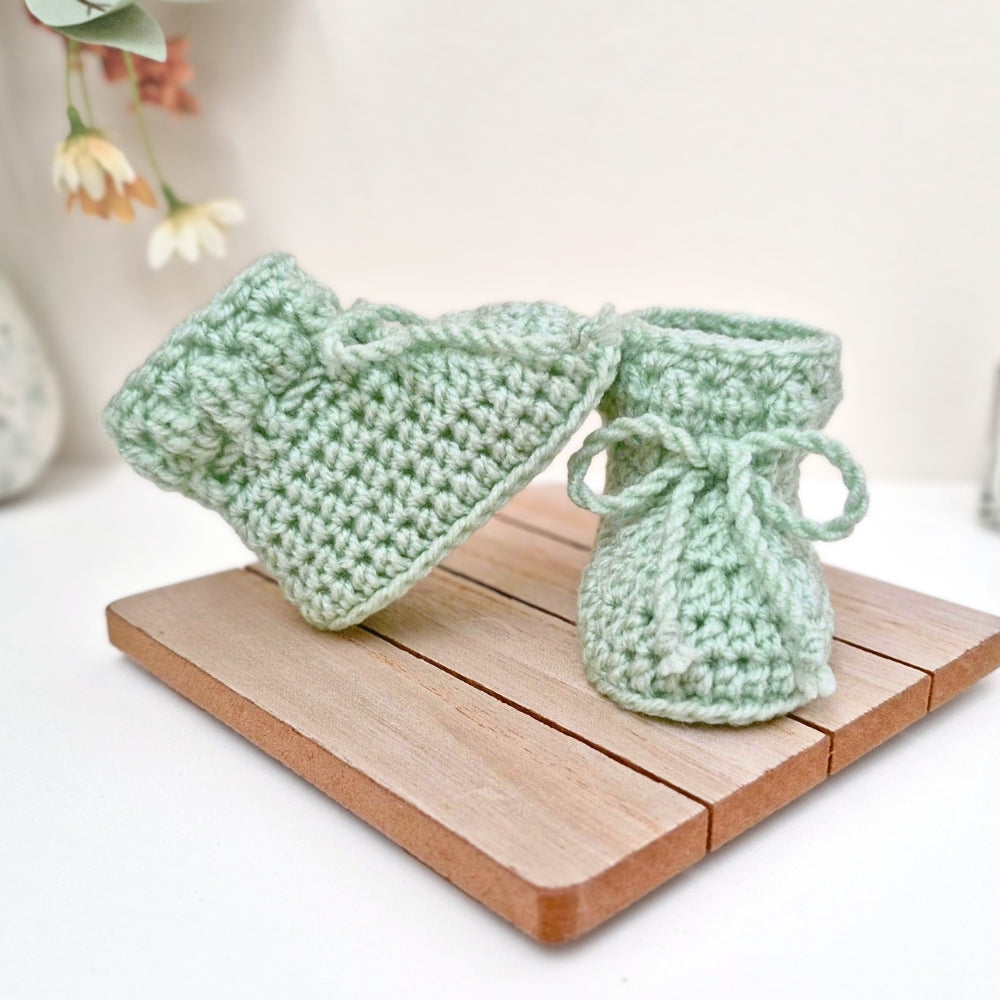 Green crocheted baby booties on a wooden coaster 
