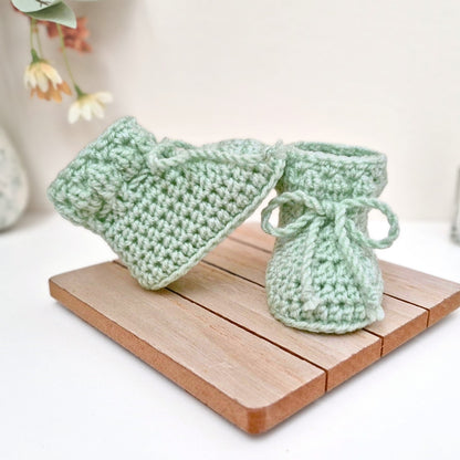 Green crocheted baby booties on a wooden coaster 