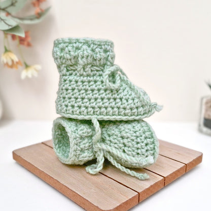 Green crochet baby booties on a wooden surface 