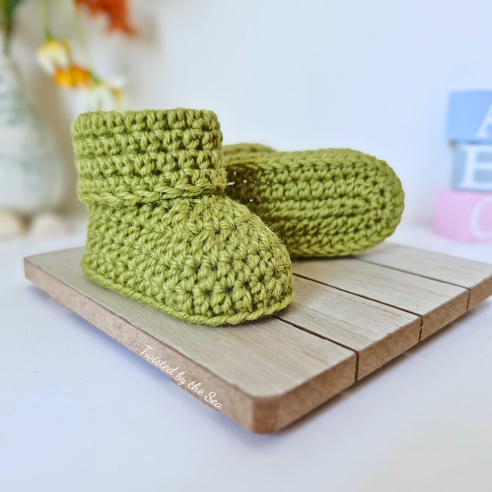 Green crochet baby boots on a wooden surface with a blurred background