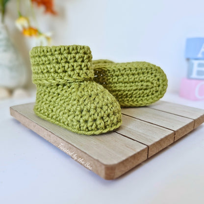 Green crochet baby boots on a wooden surface with a blurred background