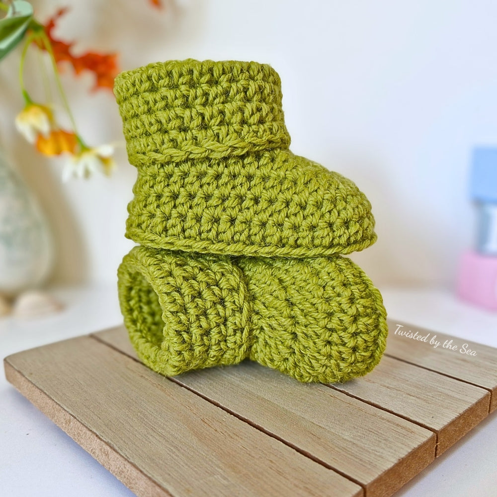 Green crochet baby booties on a wooden surface with a blurred background