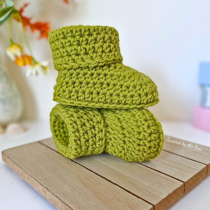 Green crochet baby booties on a wooden surface with a blurred background