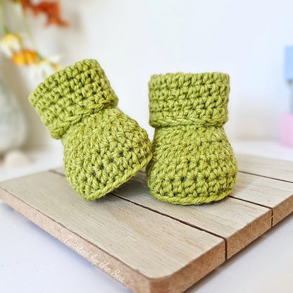 Pair of green crochet baby booties on a wooden surface with a blurred background