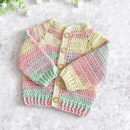A pastel crocheted cardigan sweater with horizontal stripes in pink, yellow, green, and lavender, featuring wooden buttons, laid flat on a light gray textured surface.