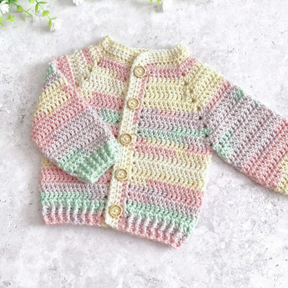 A handmade crocheted baby cardigan with pastel stripes in pink, yellow, green, and beige, featuring wooden buttons, laid flat on a light textured surface.