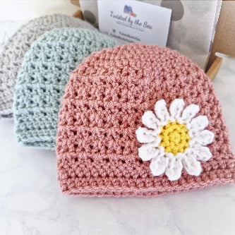 Handmade crochet baby beanie hats in pink, mint green, and beige, featuring a white daisy flower embellishment
