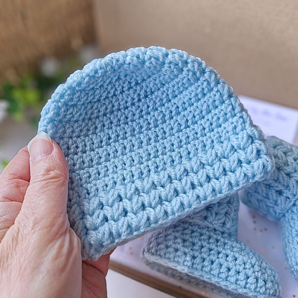 Blue crocheted baby hat held by a hand with a blurred background