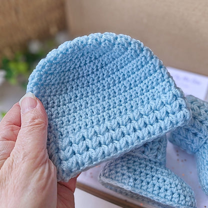 Blue crocheted baby hat held by a hand with a blurred background