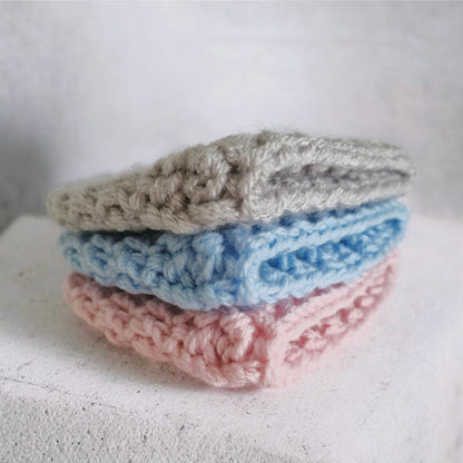 Stack of three crocheted beanie hats in gray, blue, and pink on a white surface.
